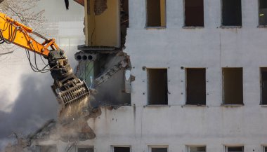 Eski bir binayı yıkan bir kazıcı kovasını kapat. Şehirde tehlikeli bir yıkım işe yarıyor. Fotoğraf güneşli bir günde çekildi..