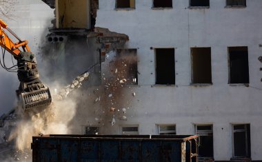 Eski bir binayı yıkan bir kazıcı kovasını kapat. Şehirde tehlikeli bir yıkım işe yarıyor. Fotoğraf güneşli bir günde çekildi..