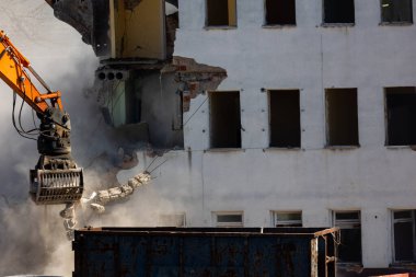 Eski bir binayı yıkan bir kazıcı kovasını kapat. Şehirde tehlikeli bir yıkım işe yarıyor. Fotoğraf güneşli bir günde çekildi..