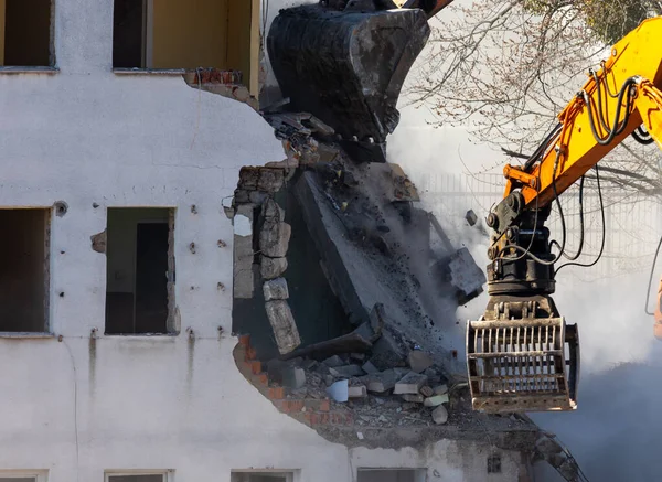 Eski bir binayı yıkan bir kazıcı kovasını kapat. Şehirde tehlikeli bir yıkım işe yarıyor. Fotoğraf güneşli bir günde çekildi..
