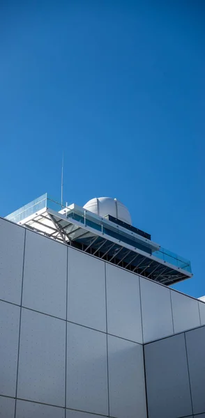 Details of a white modern public building. Sky observation tower on top of the building. Subject photographed against a blue sky on a sunny afternoon