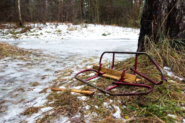 Broken children\'s snow sled lying on melting snow. Danger during snow trails. The photo was taken on a cloudy day