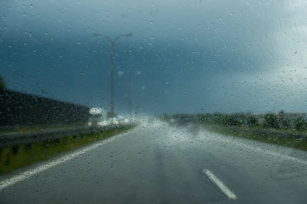 Driving the car on the highway during heavy rain. View from the front window toward the road. Windscreen full of blurry rain drops.
