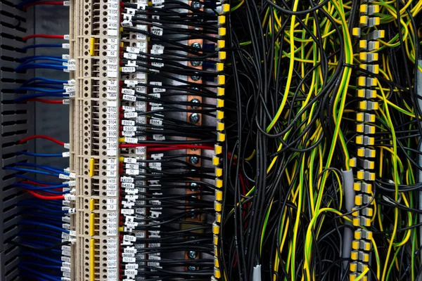 Electrical wiring harnesses connected to terminals in the control cabinet of an industrial machine. Cable ends marked with descriptions