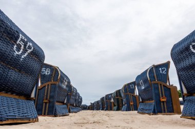 Rows of blue beach rattan huts on a beach on a cloudy day. No tourists on the beach.