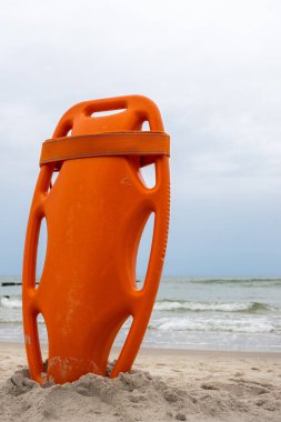 An orange lifeboat stuck in the sand on the beach. In the background, a view of the sea and clouds on the horizon