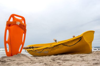 An orange lifeboat stuck in the sand on the beach. In the background, a view of the sea and clouds on the horizon