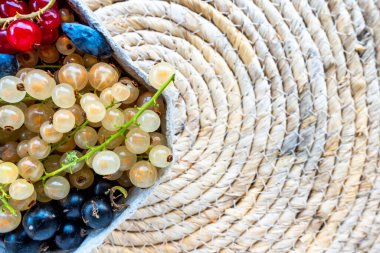 A composition of red, black and white currants in a basket on the background of a mat on the table. Natural, soft light