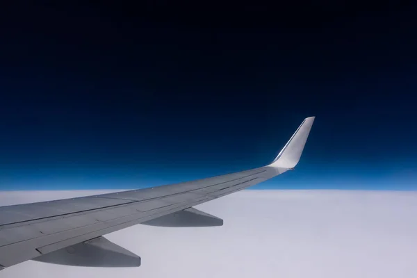 View from the plane window to the wing. Photo taken while flying above the clouds. In the distance, a visible horizon made of clouds