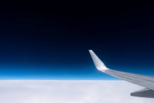 View from the plane window to the wing. Photo taken while flying above the clouds. In the distance, a visible horizon made of clouds