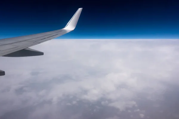 View from the plane window to the wing. Photo taken while flying above the clouds. In the distance, a visible horizon made of clouds