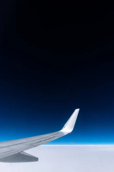 View from the plane window to the wing. Photo taken while flying above the clouds. In the distance, a visible horizon made of clouds