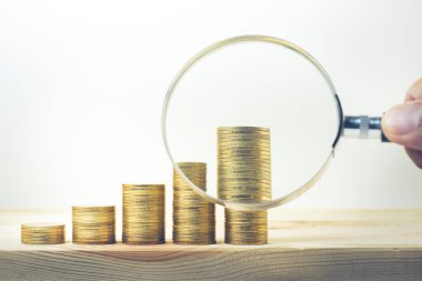 Erkek el, büyüteç ve ahşap masaya para yığılmış. İş büyümesi ve finansal konsept için.