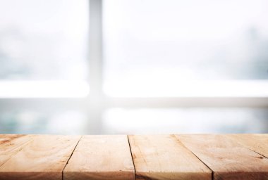 Ahşap masanın üstü soyut pencere bulanıklığı ve kış mevsiminde güneş ışığı arka planına sahip masa, kış sabahı arka planında penceresi olan masa. Montaj ürünü görüntüleme veya tasarım için görsel anahtar düzeni.