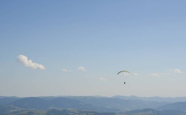 Paraglider yaz günü açık gökyüzüne karşı Karpat dağları üzerinde uçuyor