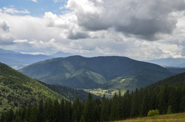 Orman, dağlar ve bulutlu gökyüzünün altındaki vadideki küçük Karpat köyü manzarası. 