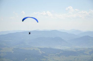 Paraglider açık havada mavi gökyüzüne karşı dağların üzerinden uçuyor. Olağanüstü spor, yaşam tarzı ve özgürlük kavramı