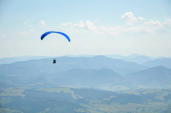 Paraglider açık havada mavi gökyüzüne karşı dağların üzerinden uçuyor. Olağanüstü spor, yaşam tarzı ve özgürlük kavramı