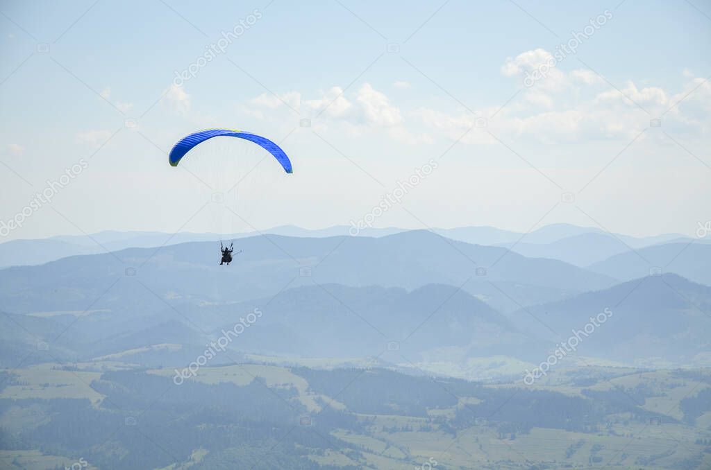 Paraglider flying over the mountains against the blue sky in clear weather. Extreme sport, lifestyle and freedom concept