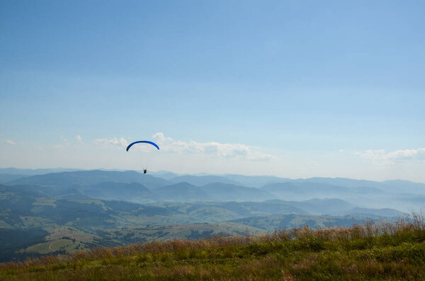 Парапланерист летит над Карпатами против ясного неба в летний день