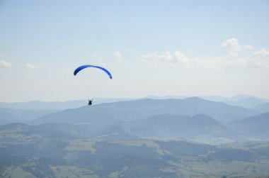 Paraglider parlak güneşli bir günde dağların üzerinden uçar. Gökyüzünde paraşütle atlıyor. Sıra dışı spor.