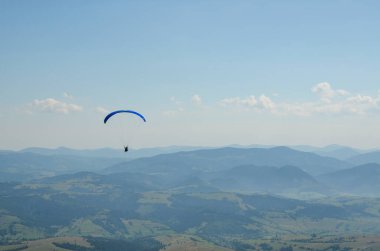 Paraglider parlak güneşli bir günde dağların üzerinden uçar. Gökyüzünde paraşütle atlıyor. Sıra dışı spor.