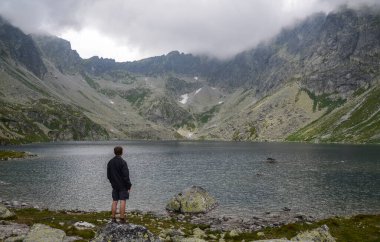 Yüksek Tatras, Slovakya 'daki Hincovo Pleso Gölü' ne ve sisli kayalık dağlara bakan bir adamın dikiz görüntüsü