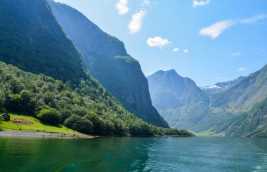Norveç 'teki Şelale ve fiyort Sognefjord Dağları. Bulutlar ve mavi gökyüzü. Güzel çarpıcı dağlar, su, gökyüzü, bulutlar ve güneş manzarası. Norveç doğası 