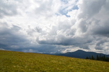 Karpatya dağları, sarı çayır, güzel gökyüzü ve bulutlar, arka planda dağ sırtı silueti. Dağların tepesinde vahşi doğa 