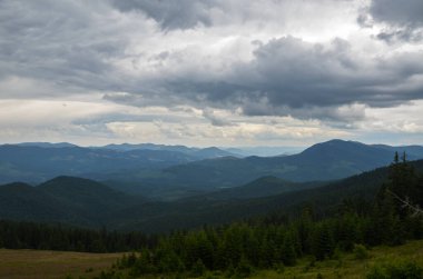Tepelerin manzarası, bulutlu gökyüzünün altındaki yeşil ormanlarla kaplı dağlar. Karpatlar, Ukrayna