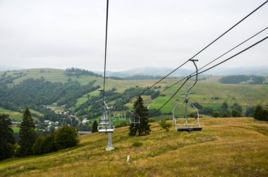 Ukrayna 'nın Karpat dağlarındaki yeşil çimenli tepenin üzerinde boş kayak kaldırma ile yaz bulutlu manzarası 