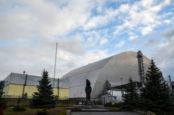 Чернобыль, Украина - 28 ноября 2020 года: Памятник и 4-й ядерный реактор под новым саркофагом в Чернобыльской зоне отчуждения, Украина