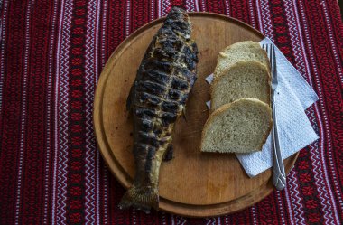 Tahta tabakta kızarmış alabalık, beyaz ekmek ve kırmızı şarap.