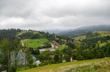 IZKY, UKRAINE - 05: 2020: sislerle kaplı bir vadide huzurlu küçük bir Karpatya köyü. Bulutlu bir günde ormanlık tepeleri olan güzel bir manzara. Karpatlar, Ukrayna