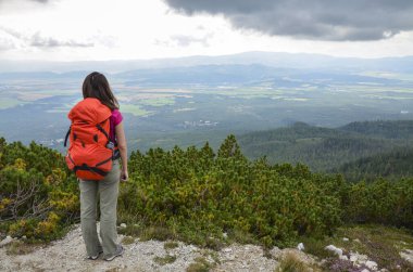 Kırmızı sırt çantalı turist kızın arka manzarası vadide nefes kesen manzaranın tadını çıkarıyor. Turizm ve seyahat kavramı.