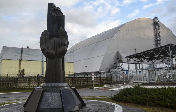 CHERNOBYL, UKRAINE - NOVEMBER 28, 2020: Monument and 4th nuclear reactor under new sarcophagus in Chernobyl Exclusion Zone, Ukraine
