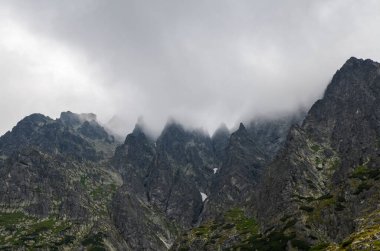 Slovakya 'daki Ulusal Park Yüksek Tatras Dağları' nda bulutlu gökyüzü altında yüksek taş gibi kayalık tepeleri olan manzara. Yürüyüş ve turizm için turizm beldesi