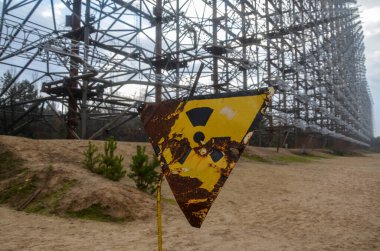 Old yellow radiation warning sign against the military Duga Radar antenna complex. Chornobyl Exclusion Zone, Ukraine.
