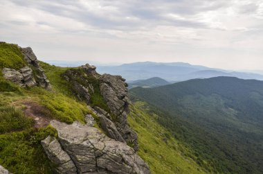 Mountain peak with boulders and forested hills on background at summer day. Pikuj mount, Carpathian mountains, U