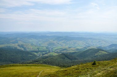 Mountain countryside landscape with grassy field on hillside and village down in the valle. Carpathian Mountains, Ukraine