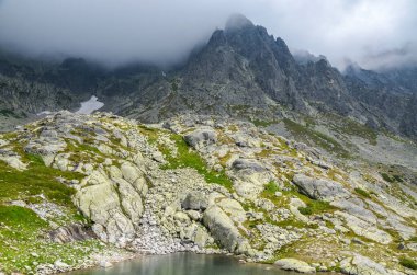 Sisli ve keskin tepeler yukarıdaki sislerin arasından yükseliyor ve Slovakya 'daki High Tatras Ulusal Parkı' nda yağmur bulutları yağıyor.