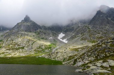 Slovakya 'daki High Tatras Ulusal Parkı' nda güzel bir dağ gölü manzarası ve bulutlu gökyüzünün altındaki kayalar.