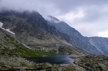 Slovakya 'daki High Tatras Ulusal Parkı' nda güzel bir dağ gölü manzarası ve bulutlu gökyüzünün altındaki kayalar.