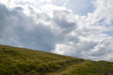 Yazın güzel dağ manzarası. Yeşil çimenler, kırsal yol ve arka planda muhteşem bir gökyüzü. Karpat Dağları, Ukrayna