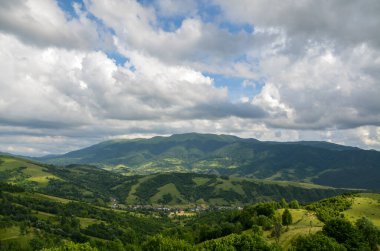 Yeşil tepelerdeki küçük bir köyün kırsal evlerinin olduğu yuvarlanan bir kırsal bölgenin resimli yaz manzarası. Karpat Dağları, Ukrayna 