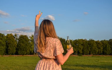 Arkadan bak. İçki şişeli kız barış işareti gösteriyor. Yaz tatili