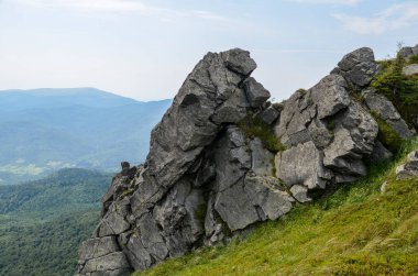 Pikuy tepelerindeki kayalar yemyeşil otlarla kaplı dağların arasında. Yazın bulutlu bir gün. Ukrayna, Karpat Dağları, Lviv Bölgesi
