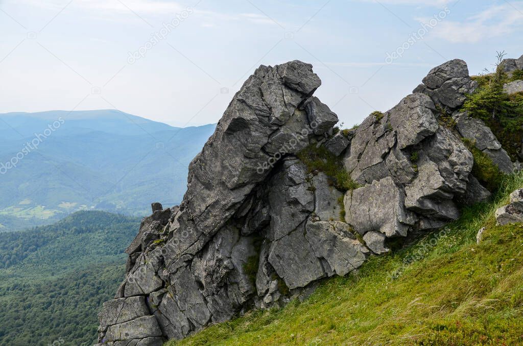 Rocks on Pikuy mount among green mountain hills covered in lush grass. Cloudy day in summer. Ukraine, Carpathian Mountains, Lviv region