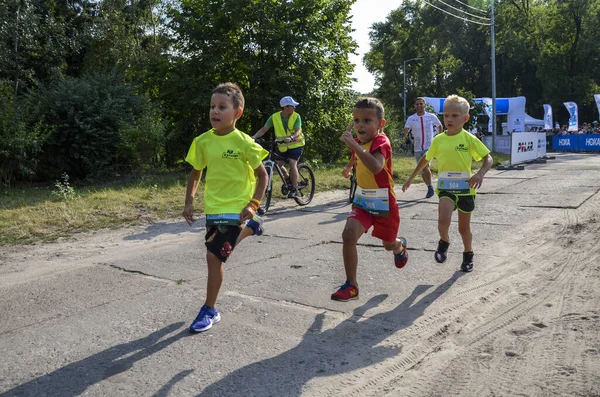 KYIV, UKRAINE - 24 Temmuz 2021: Çocuklar şehir parkında açık pistte koşuyorlar. Çocuklar için sağlıklı spor aktiviteleri. Atletizm yarışındaki küçük çocuklar. Eğitimdeki genç bir atlet. Çocuk için koşmak.