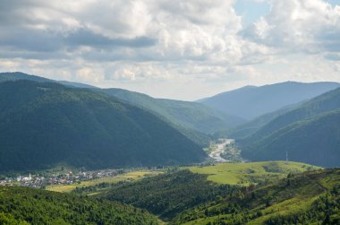 River flowing through mountain valley covered with dense forests under cloudy sky. Carpathian mountains, Ukraine